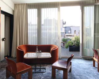 Hotel suite with balcony, with burnt red couch, accent chairs surrounding marble coffee table