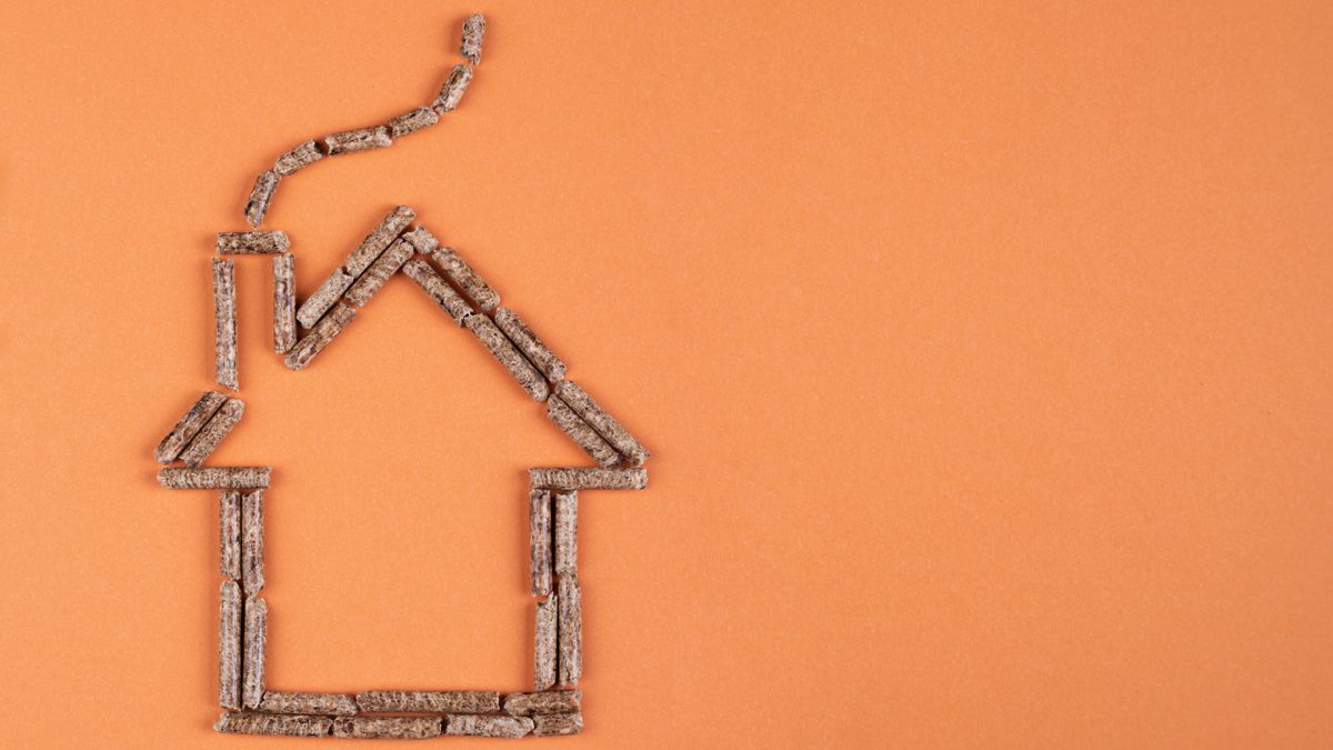 orange background with wooden biomass boiler pellets arranged in shape of a house