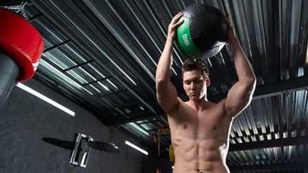 Waist-up portrait of serious muscular man doing standing overhead medicine ball slam