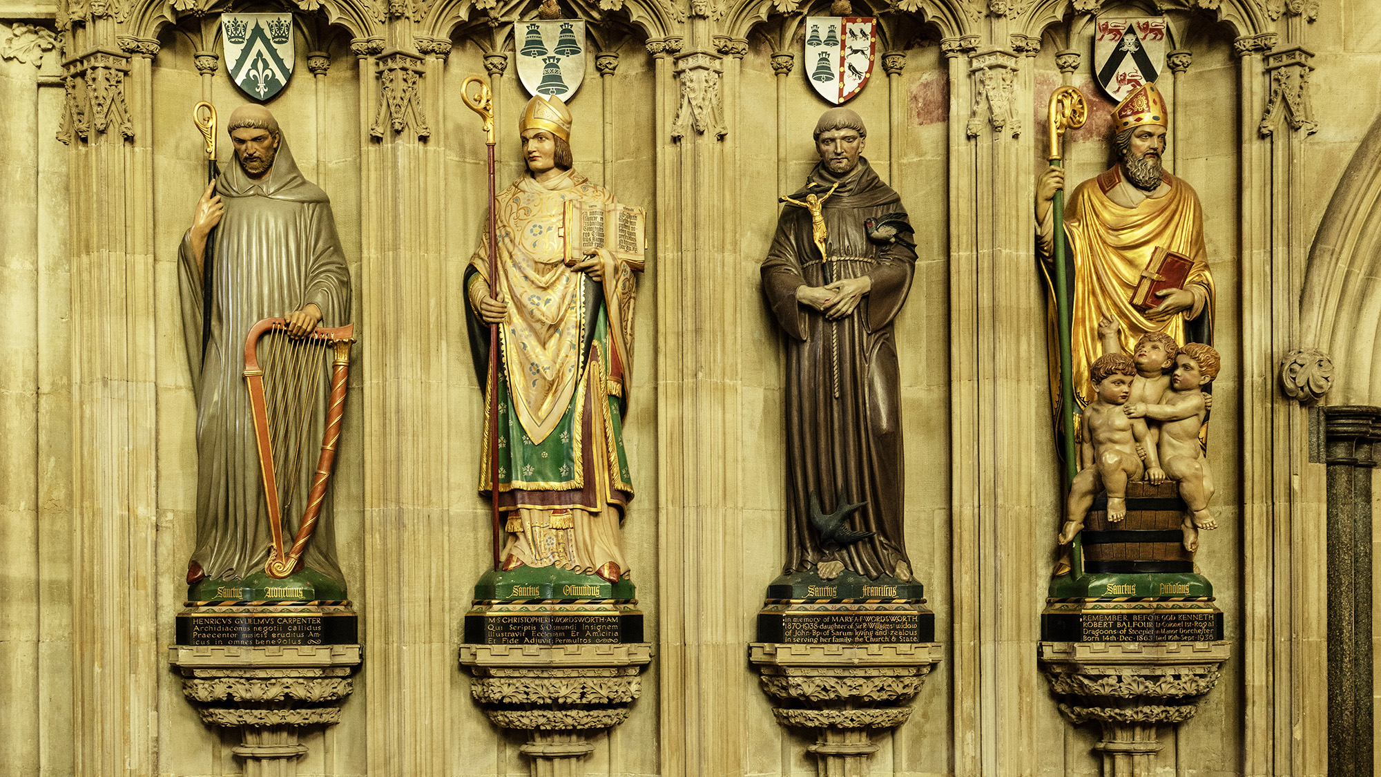 Four religious figures in a line with coat of arms on a shield above