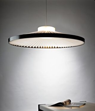 A suspension light with with a full circular fan-like lampshade and a black rim.