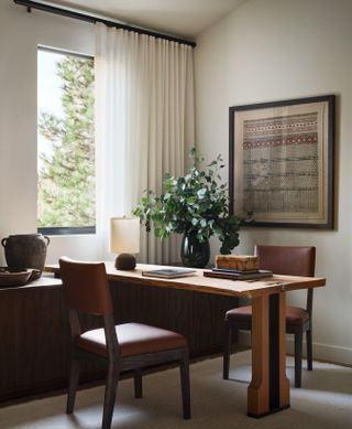 A clean and minimal office with artwork hanging on the wall and a plant and vase sits in the corner of a room