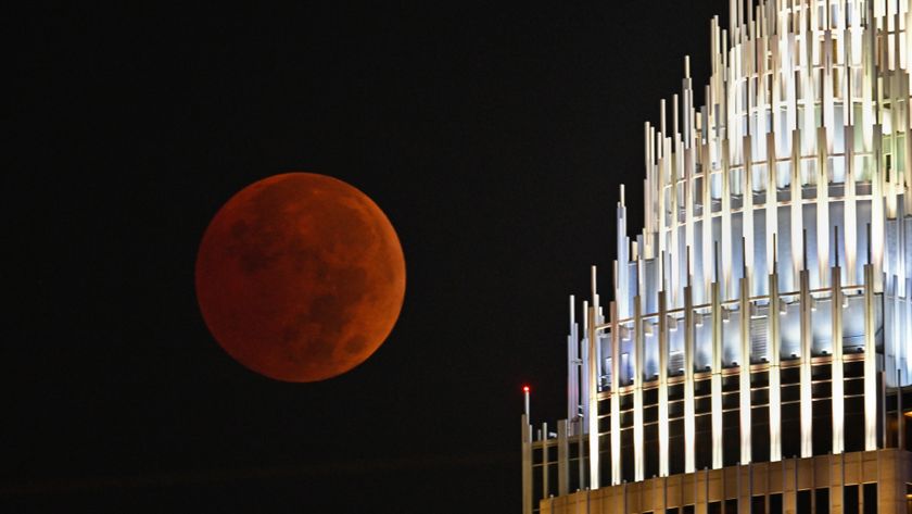 a blood red moon during a total lunar eclipse on the left and a building illuminated on the right