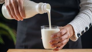 person pouring a kefir drink from a bottle into a glass