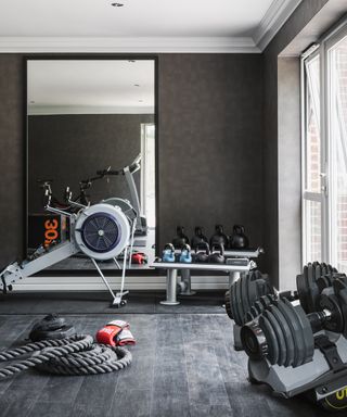 A grey gym with rowing machine and large black framed mirror