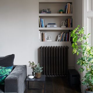 A living room with a grey velvet sofa and a black radiator