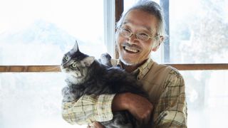 An elderly man smiles as he holds a large-breed cat