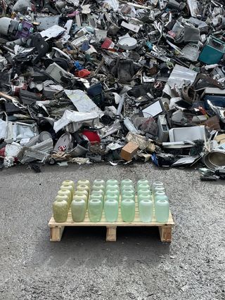 Glass jars in shades of light green with pile of waste in background