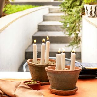 Candle planters using terracotta pots to make a simple patio display, a table with crockery and cutlery outdoors, with lit candles in old terracotta pots.