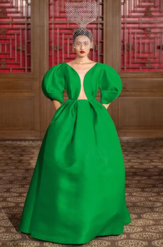 View of a model walking the Valentino Beijing Haute Couture 2019 show - the model is wearing a green floor length dress and has a semi transparent embellished structure on her head which covers half of her face and extends upwards