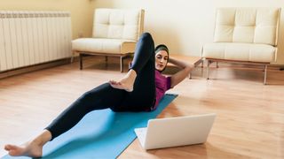 Woman doing bicycle crunches on yoga mat at home with laptop