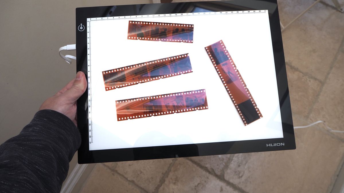 35mm film negatives on a Huion L4S light pad held in a hand