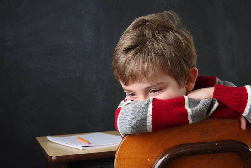 A boy slumps at his school desk, hiding his face.