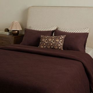 bed with dark brown bedding and patterned cushion