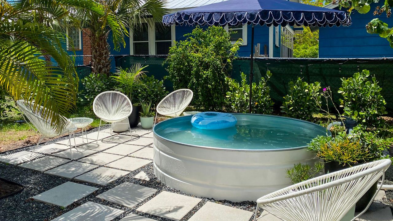 white painted stock tank pool on a backyard patio with blue parasol overhead