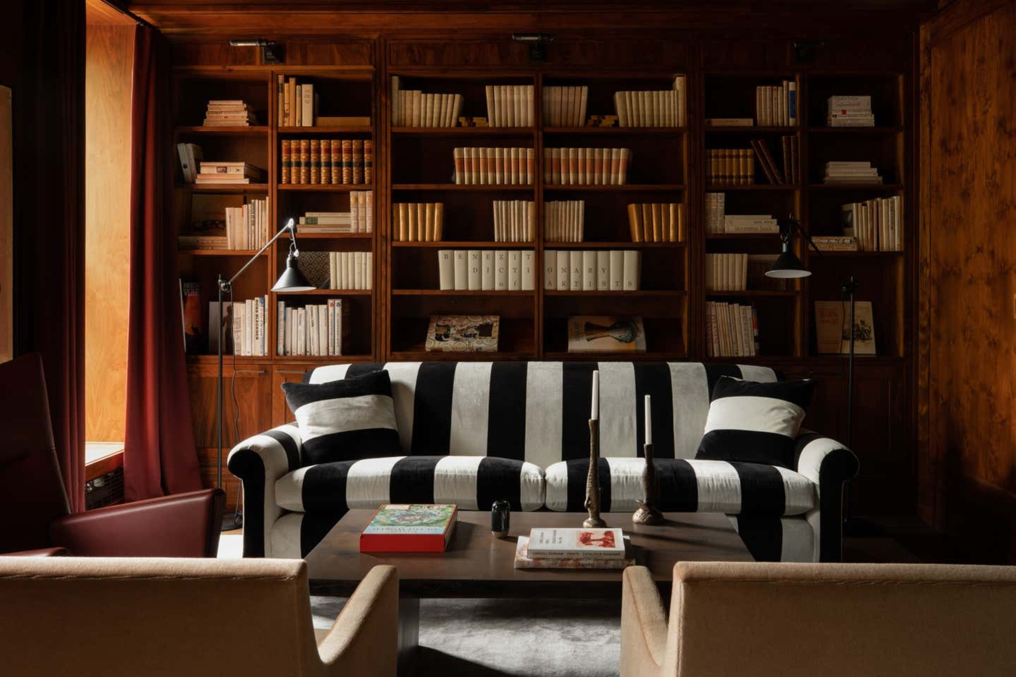A black and white striped sofa in a library room that is drenched in dark wood. There is a wall-to-wall bookshelf.