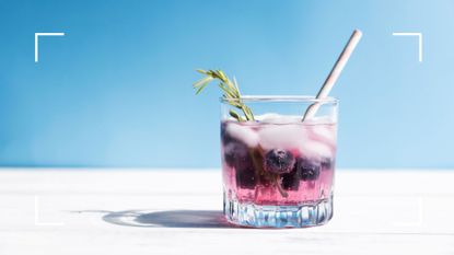 Drink with rosemary and berries in glass with white straw, an example of healthy alcohol, on white and blue background