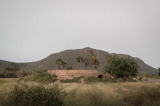 minimalist spiritual enclosure structure in pink hue concrete among desert green nature