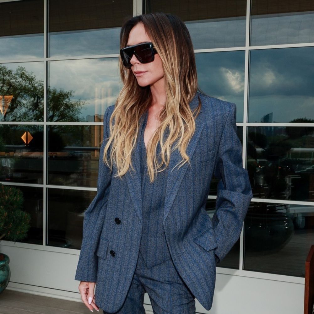 Victoria Beckham wears a striped suit with patent leather croc print heels and oversized sunglasses.