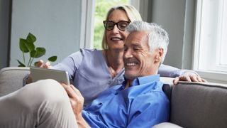 Older healthy couple sit on sofa together