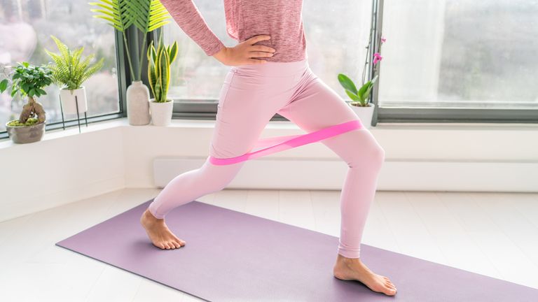 Woman lunging forward with a pink resistance band around her thighs