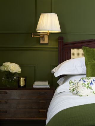 green bedroom with swivel arm wall light, mahogany furniture, green throw, cushion, floral cushion, white bedding