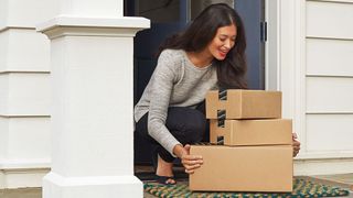 A woman smiling while she picked up three Amazon boxes from her doorstep