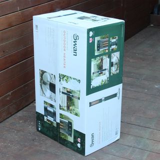 The Swan Column patio heater in its green and white packaging box on wooden decking