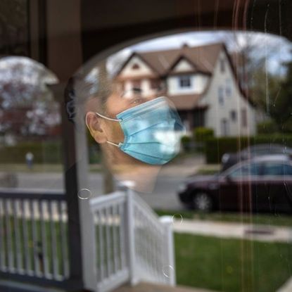 A woman wearing a surgical mask looks out of a window.