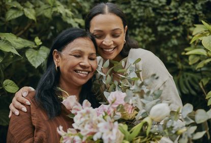 A mother and daughter happily holding each other with a bouquet of flowers for Mother's Day.