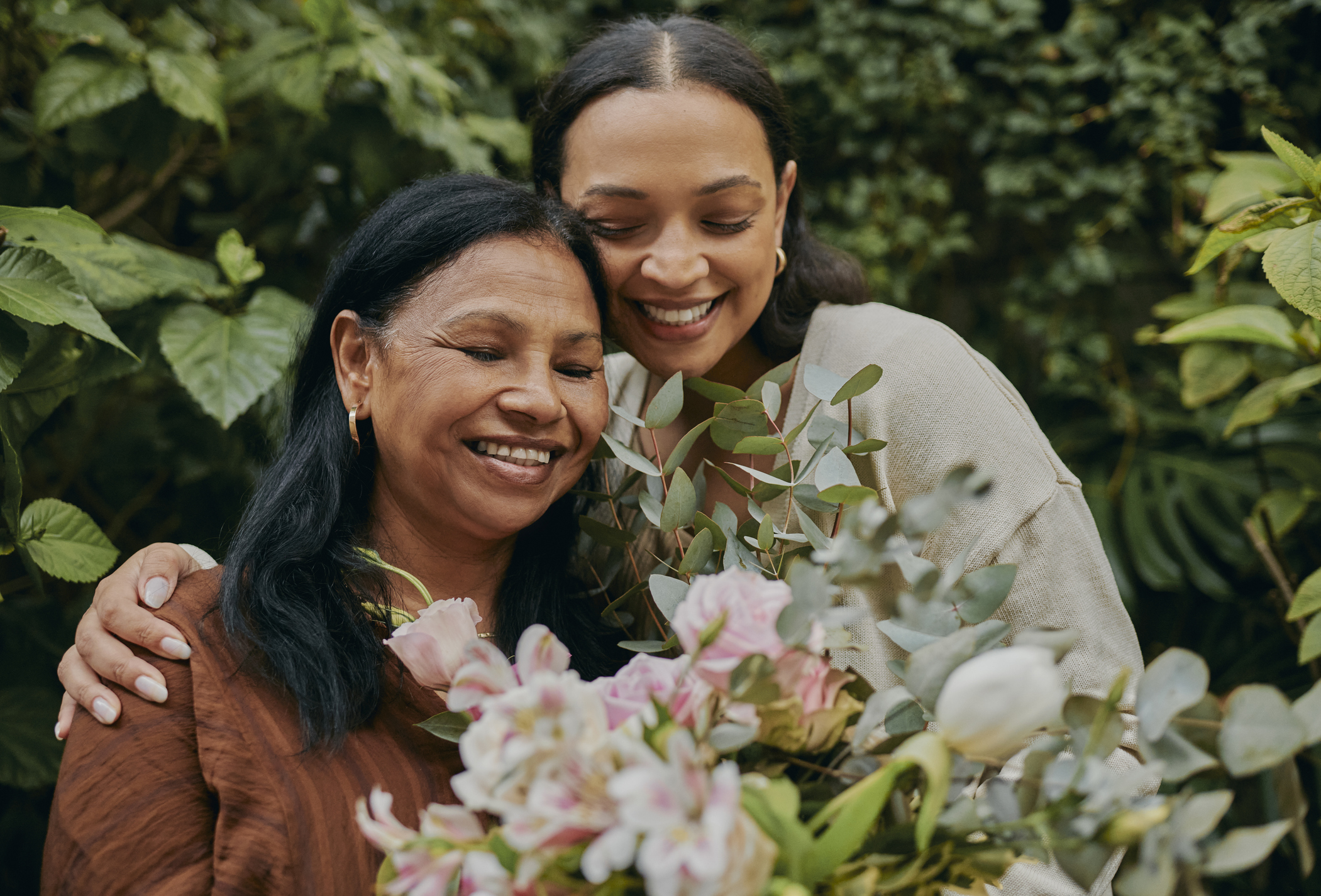 A mother and daughter happily holding each other with a bouquet of flowers for Mother's Day.