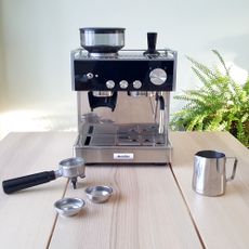 The black and stainless steel Breville Barista Signature Espresso Machine with a portafilter and stainless steel milk jug on a wooden table