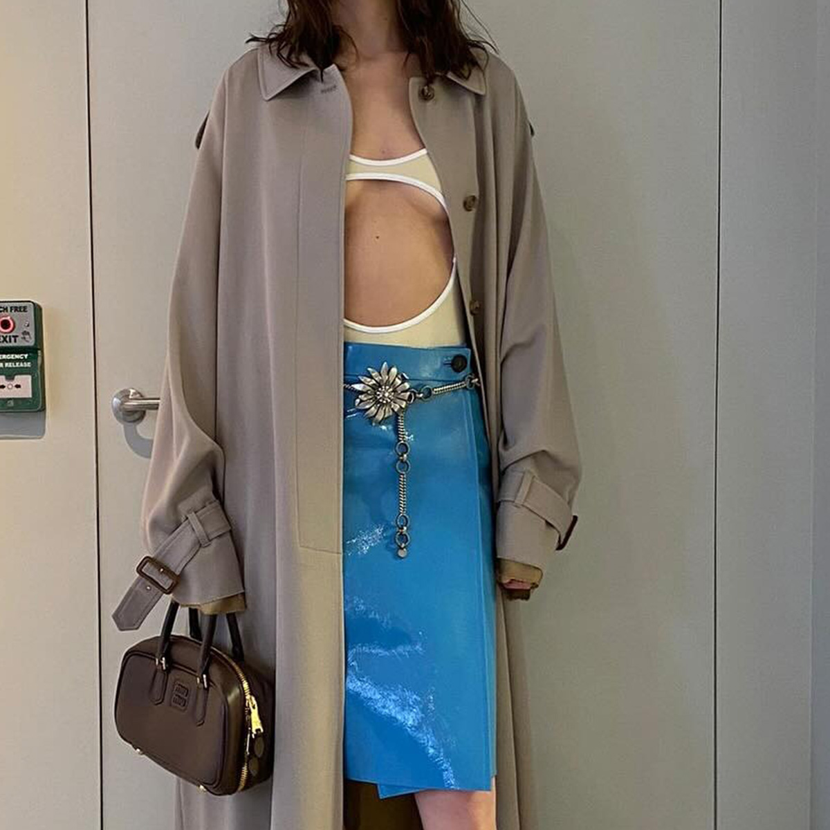 Alexa Chung wearing a trench coat with a swimsuit and patent leather blue Miu Miu skirt with knee-high suit socks and gold peep-toe heels.