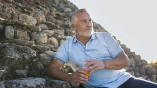 Paul Hollywood in a blue shirt holding a drink in a plastic cup in Mexico in Paul Hollywood Eats Mexico.