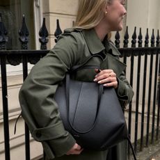 Woman wears green trench coat and carries black bag