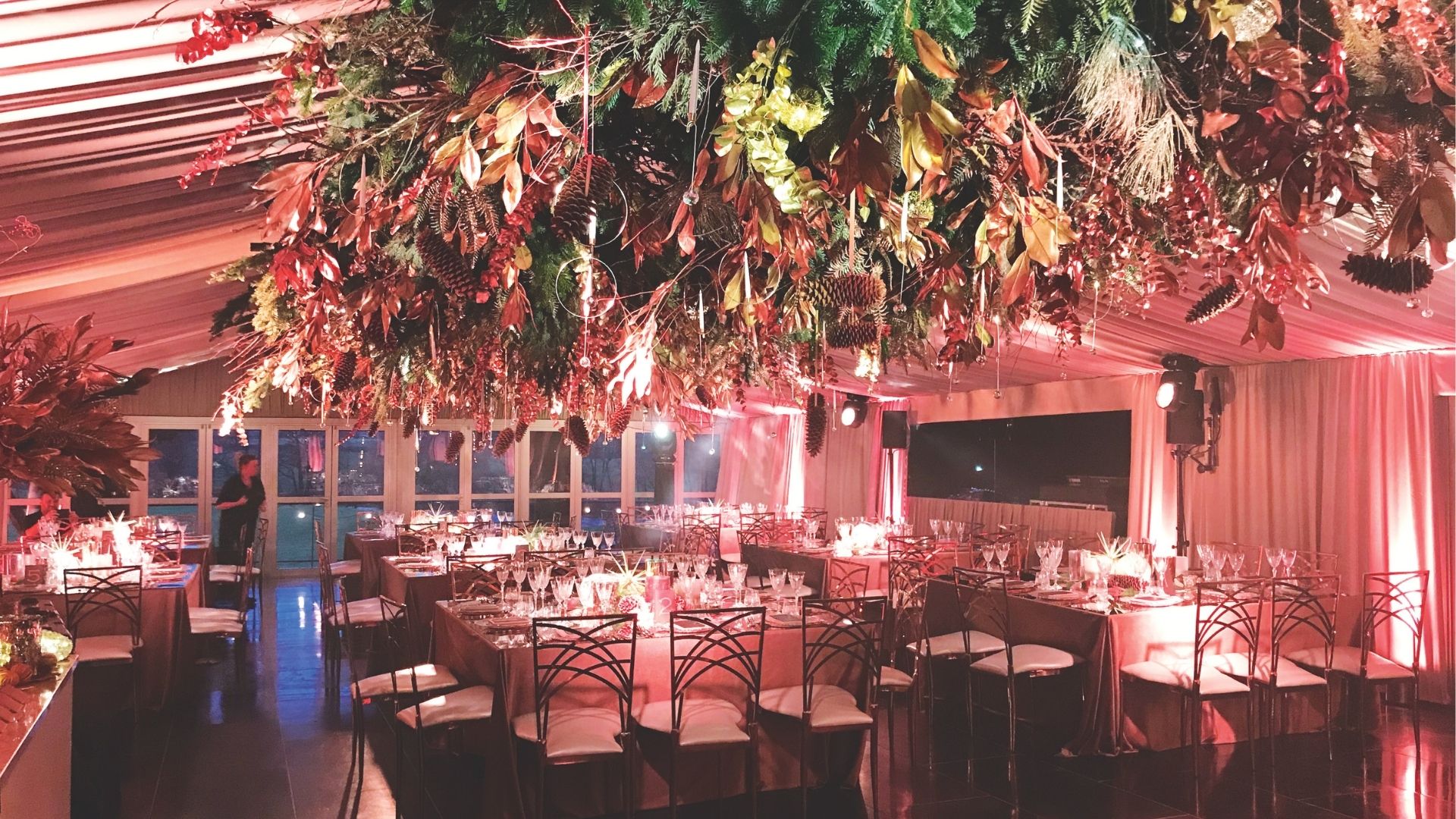 At one of Liz Taylor&#039;s extravagant Christmas parties for a client, Christmas tree foliage and decorations are seen hanging from the ceiling, above dining tables, chairs and a bar