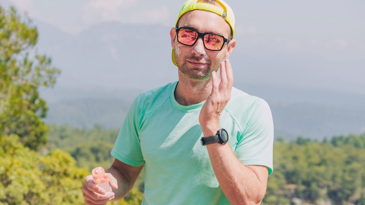 Runner wearing sunglasses, baseball cap and T-shirt applying sunscreen to face