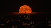 A red moon shines over an Italian toen in a black sky.
