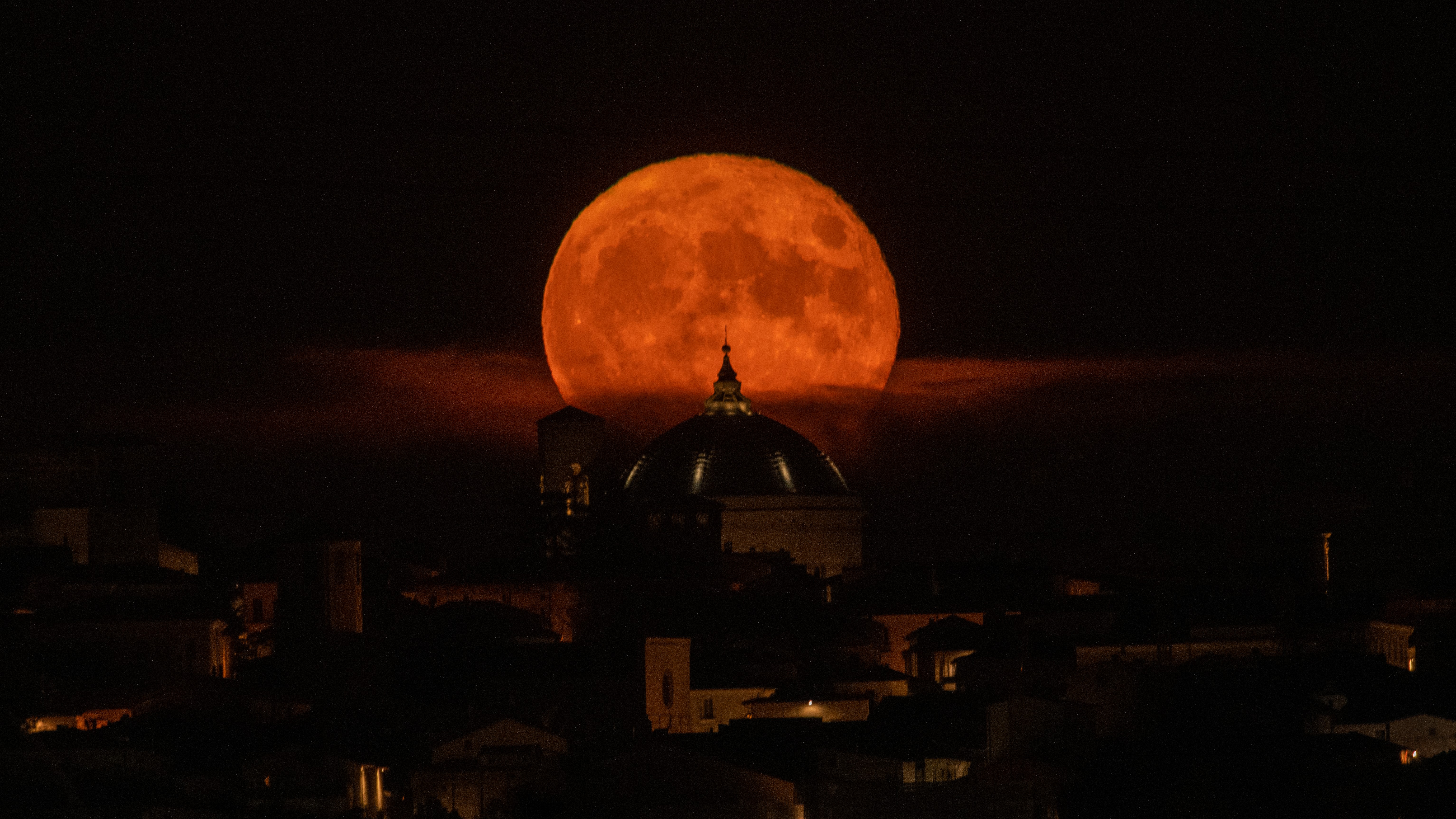 A red moon shines over an Italian toen in a black sky.