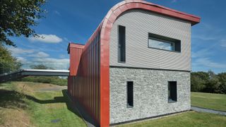 self build with grey stone clad exterior and corten steel curved roof and back wall
