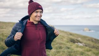 A hiker by the sea unzips his down jacket that he's wearing over a fleece