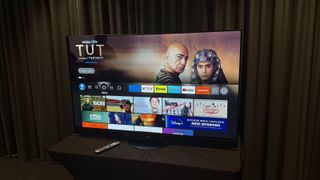 Panasonic Z95A TV photographed against a grey curtain. On the screen is the Amazon Fire OS homescreen.