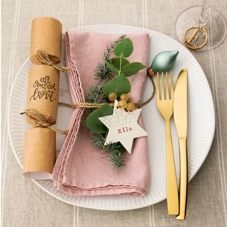 pink folded Christmas napkin tied with twine placed on white plate next to gold knife and fork
