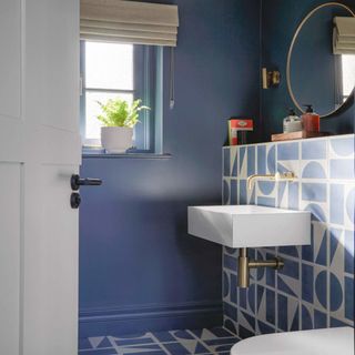 downstairs toilet with blue and white patterned tiles, white basin, circular mirror and shelving with books and hand wash