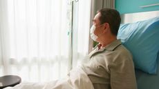 man lying in bed with intravenous injection is looking through window and wearing face mask at hospital
