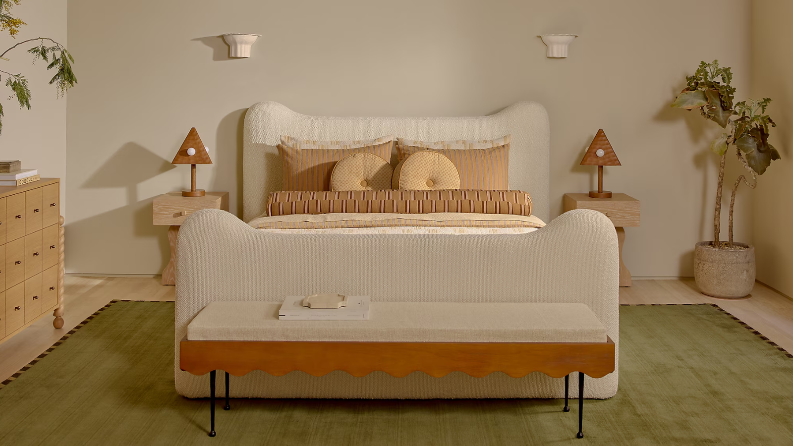 a warm, whimsical bedroom with a green rug, a white upholstered bed, a bench at the foot of the bed, and pillows on the bed