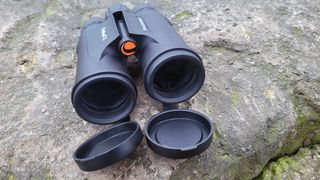 Celestron Outland X 10x42 binoculars with lens caps off, on a rock