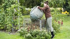 Female gardener adding green waste to a garden compost heap