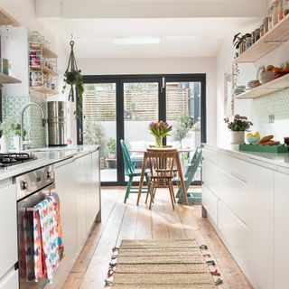 White galley kitchen with open shelving and small wooden dining table
