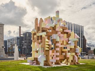Daytime exterior image, colourful design installation in tallinn park with modern city in the background, during Tallinn Architecture Biennale 2022, green lawn, buildings in the backdrop, cloudy sky